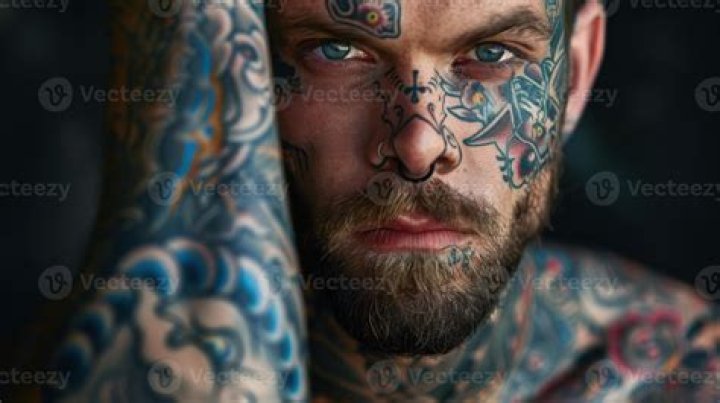 a man with tattoos on his arm holding a cell phone while standing in
